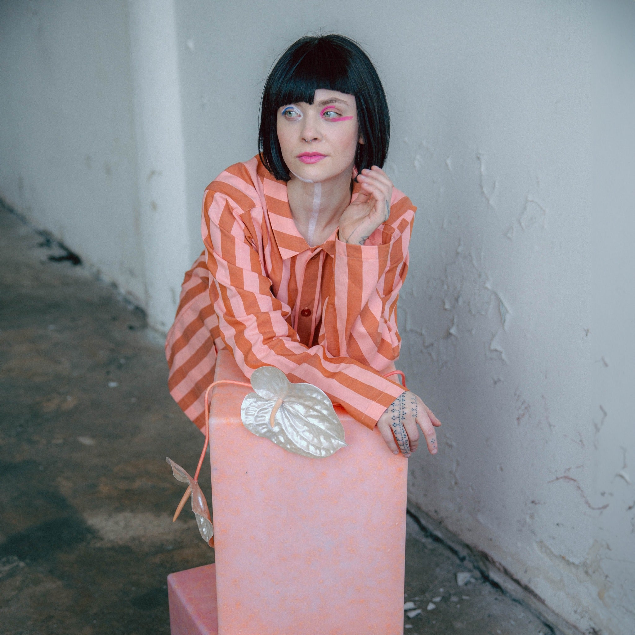 Model sitting beside the SMALLrevolution Sigrid42 podium in pink, crafted in Denmark from 100% recycled plastic waste.